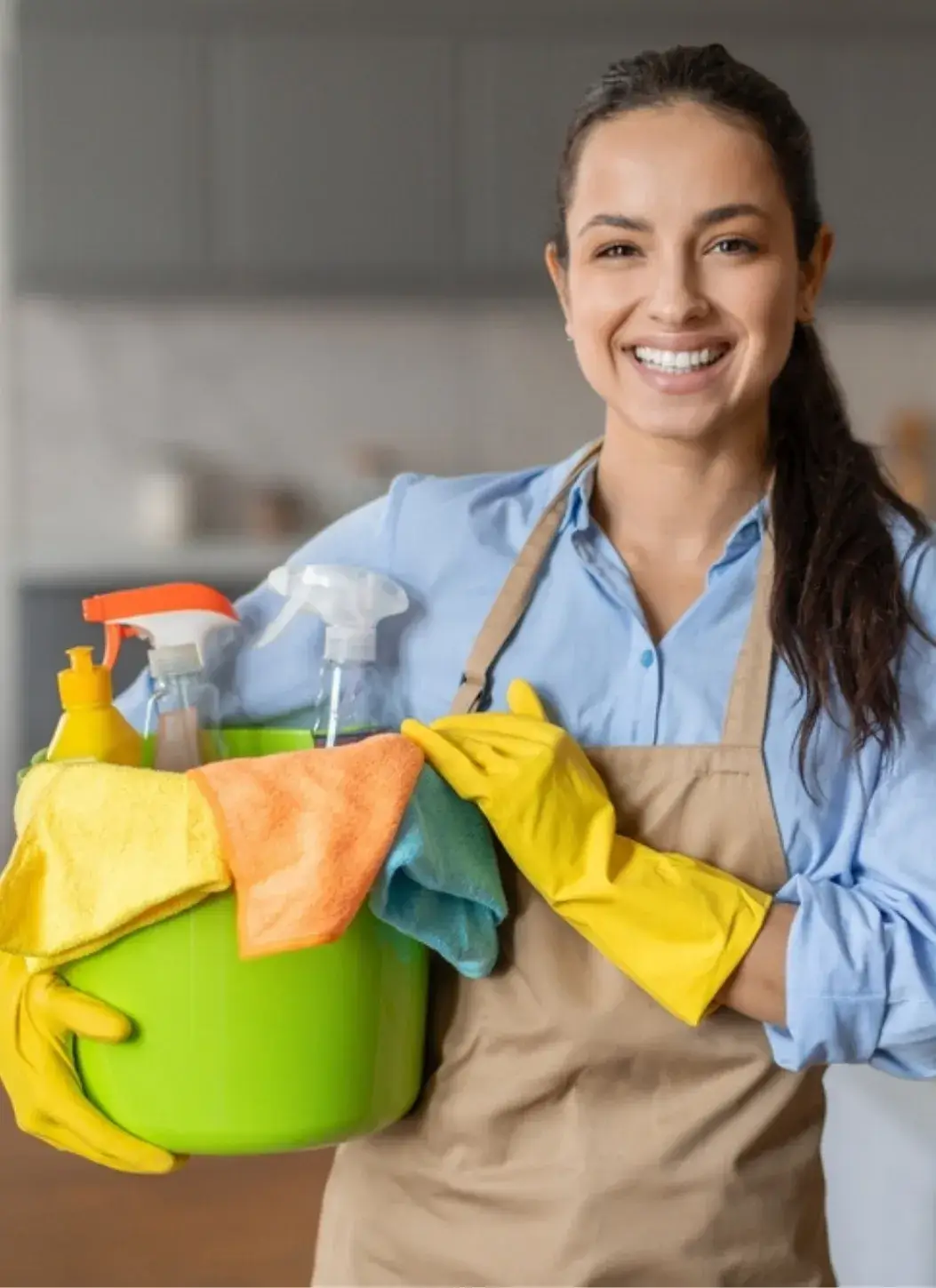 Smiling professional cleaner holding a green bucket with cleaning supplies and colorful cloths